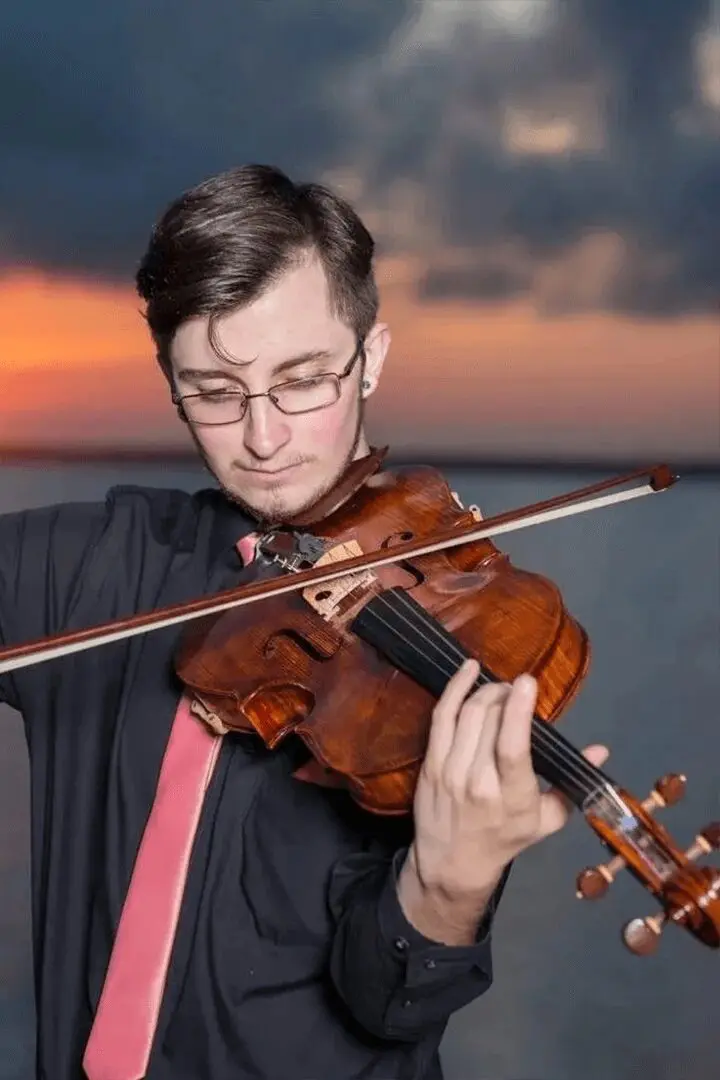 A man holding a violin in front of the ocean.